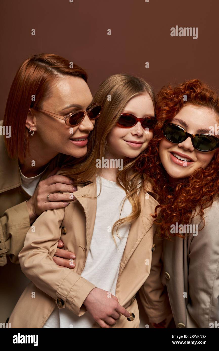 family generation change concept, cheerful redhead women and girl in sunglasses on brown