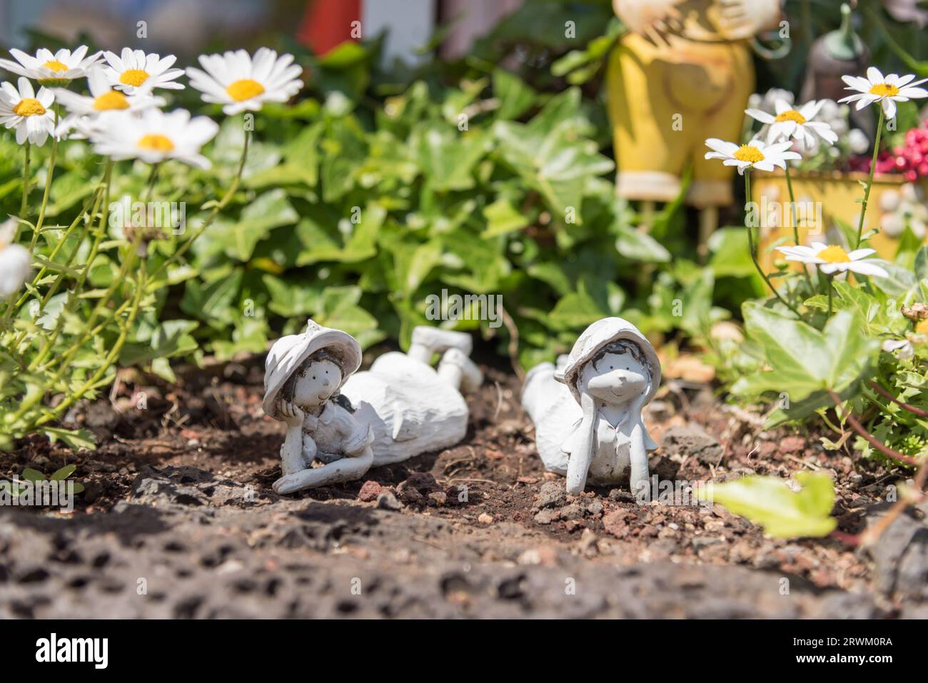 Two small sculptures of two girls laying on the ground, amongst a bed of daisies Stock Photo