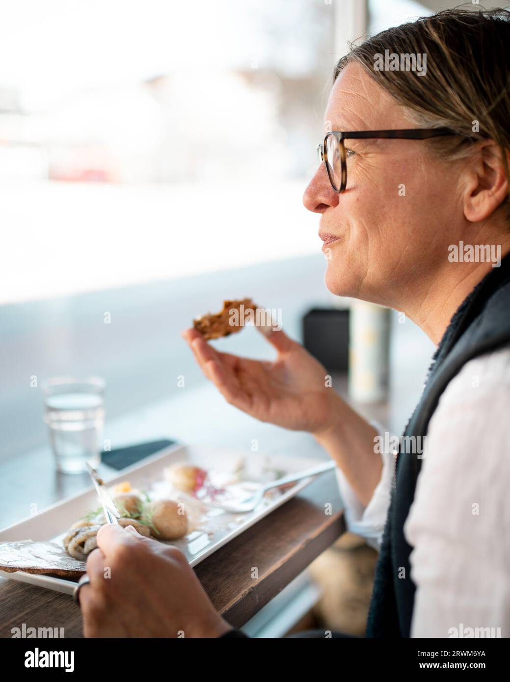 Woman sitting at a restaurant window eating. Stock Photo