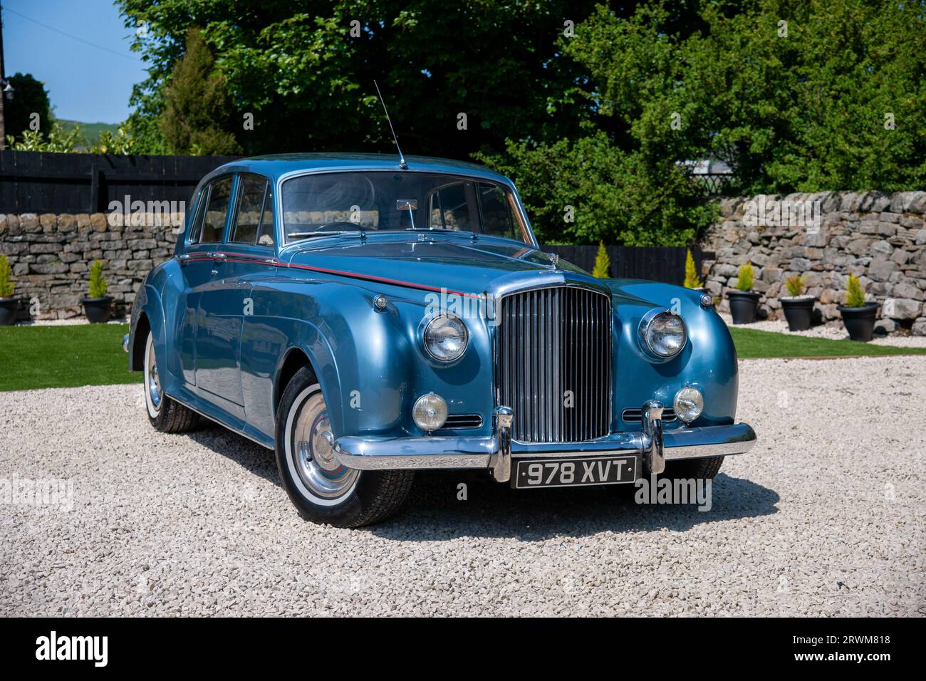 Bentley S2 four-door saloon parked in a rural setting on a gravel drive with a dry stone  and trees behind on a summer day Stock Photo