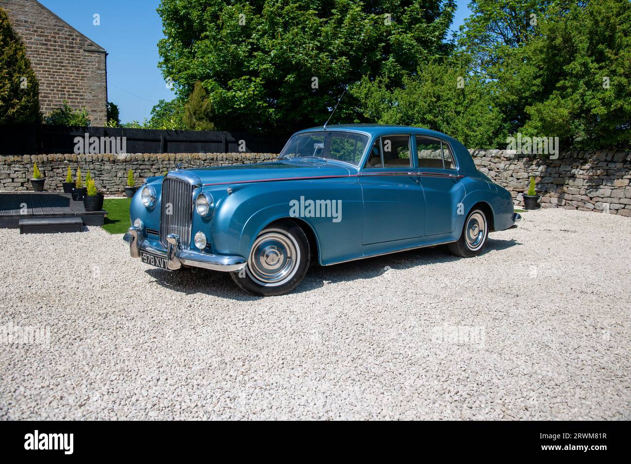 Bentley S2 four-door saloon parked in a rural setting on a gravel drive with a dry stone  and trees behind on a summer day Stock Photo
