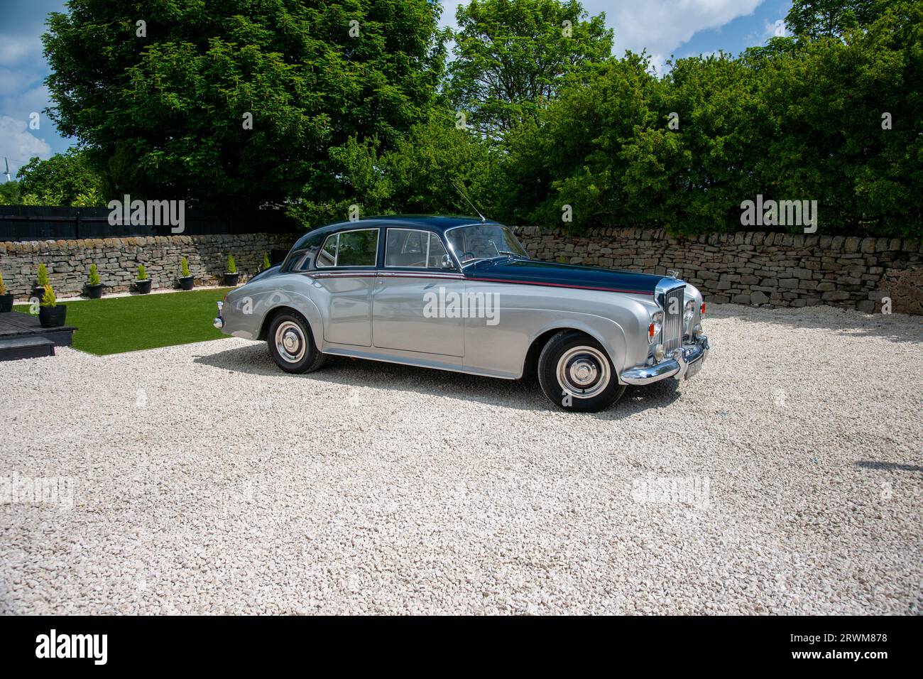 Bentley S3 parked in a rural setting on a gravel drive with a dry stone  and trees behind on a summer day Stock Photo