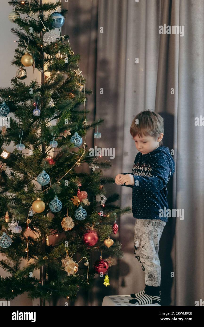 Little cute caucasian boy decorating Christmas tree with twinkling