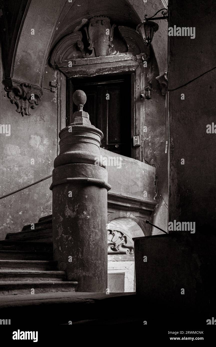 An old and weathered wooden stairway in a city setting, with a door ajar and a single lightbulb illuminating the area Stock Photo
