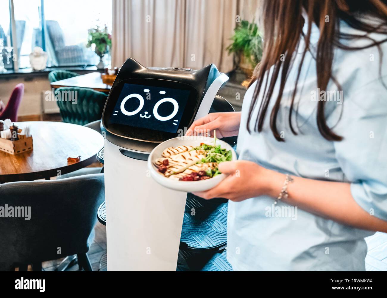 Robot waiter serve food at modern restaurant table.Offering innovation futuristic high-tech automated dining experience.Bringing,delivery automation o Stock Photo