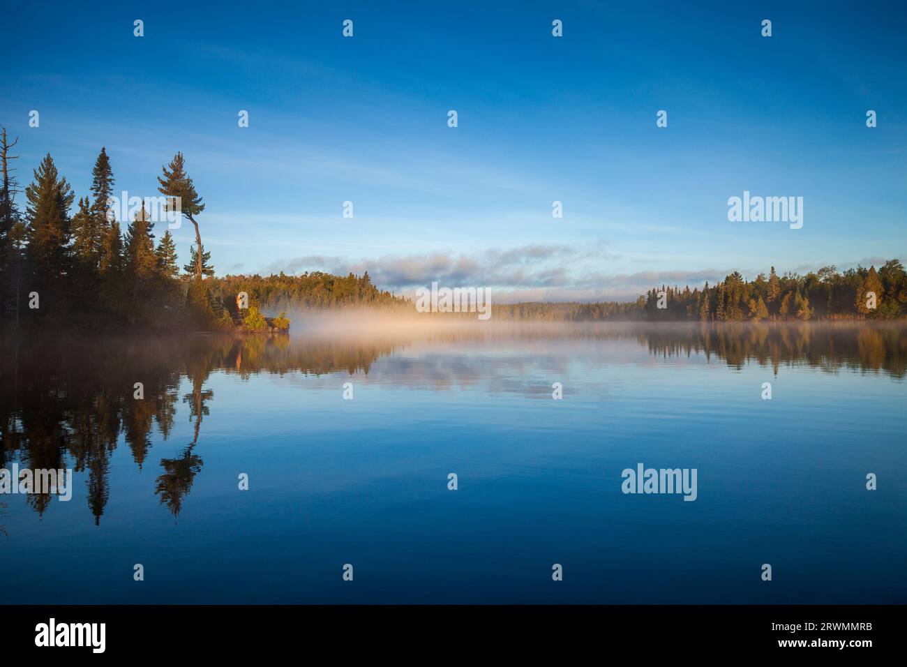 Beautiful blue lake with trees on a foggy morning in northern Minnesota at sunrise in September Stock Photo