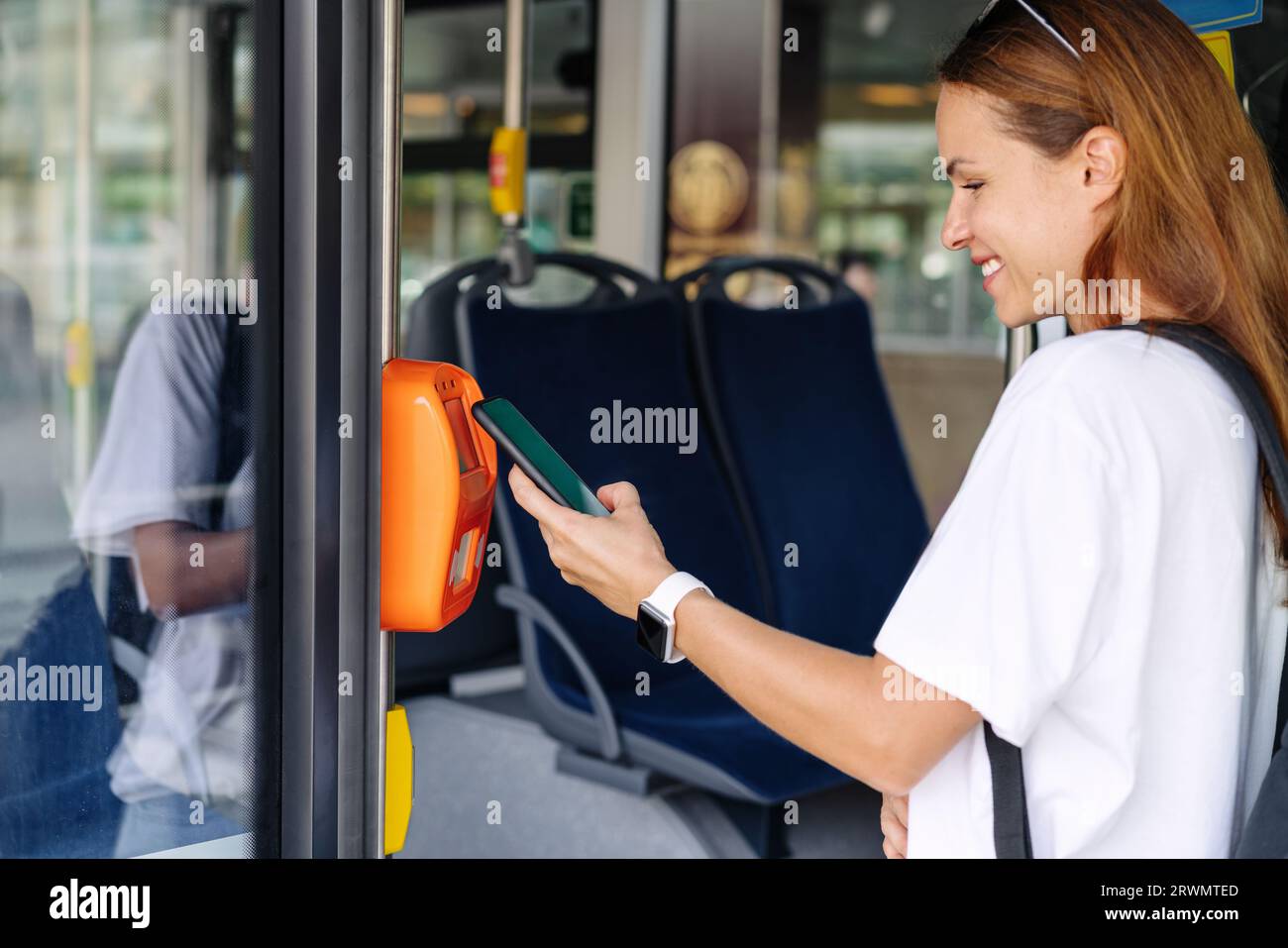 Attractive young woman paying shuttle bus using her mobile phone, contactless technology of payment in public transport. Stock Photo