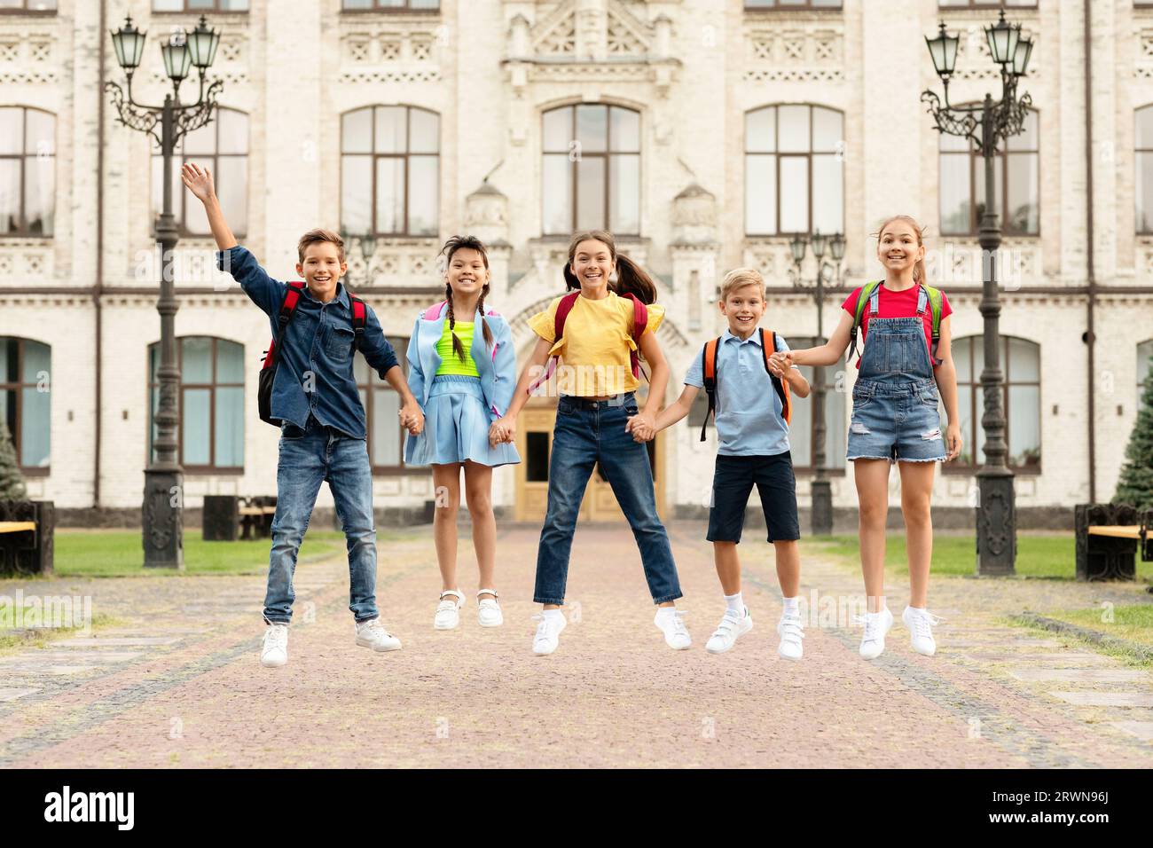 Happy Group Of Kids With Backpacks Holding Hands And Jumping Together ...