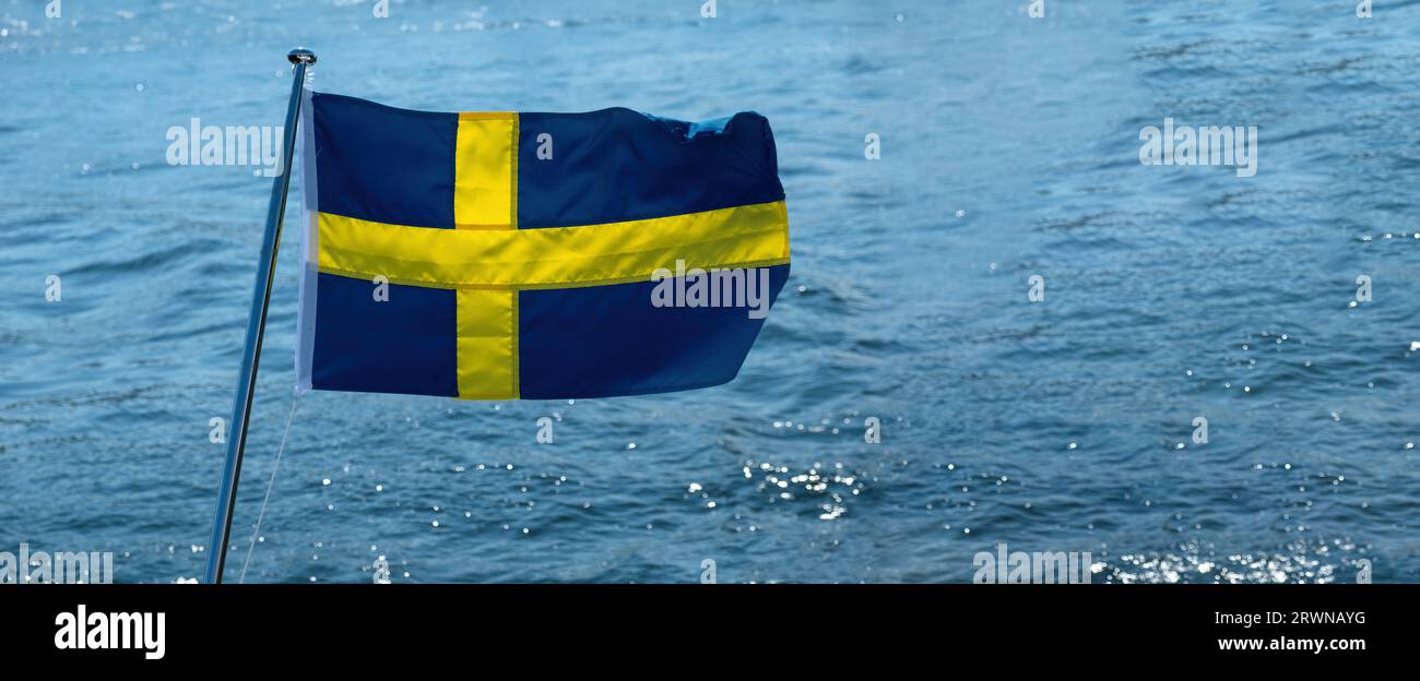 Sweden national flag waving on boat flagpole, blur sea water background, sunny day, Stock Photo