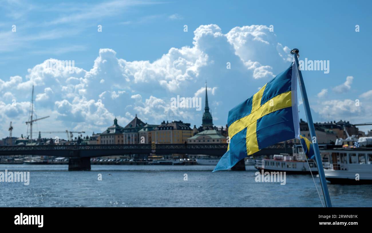 Sweden national flag waving, blur waterfront Stockholm buildings and blue sky background, sunny day, Stock Photo