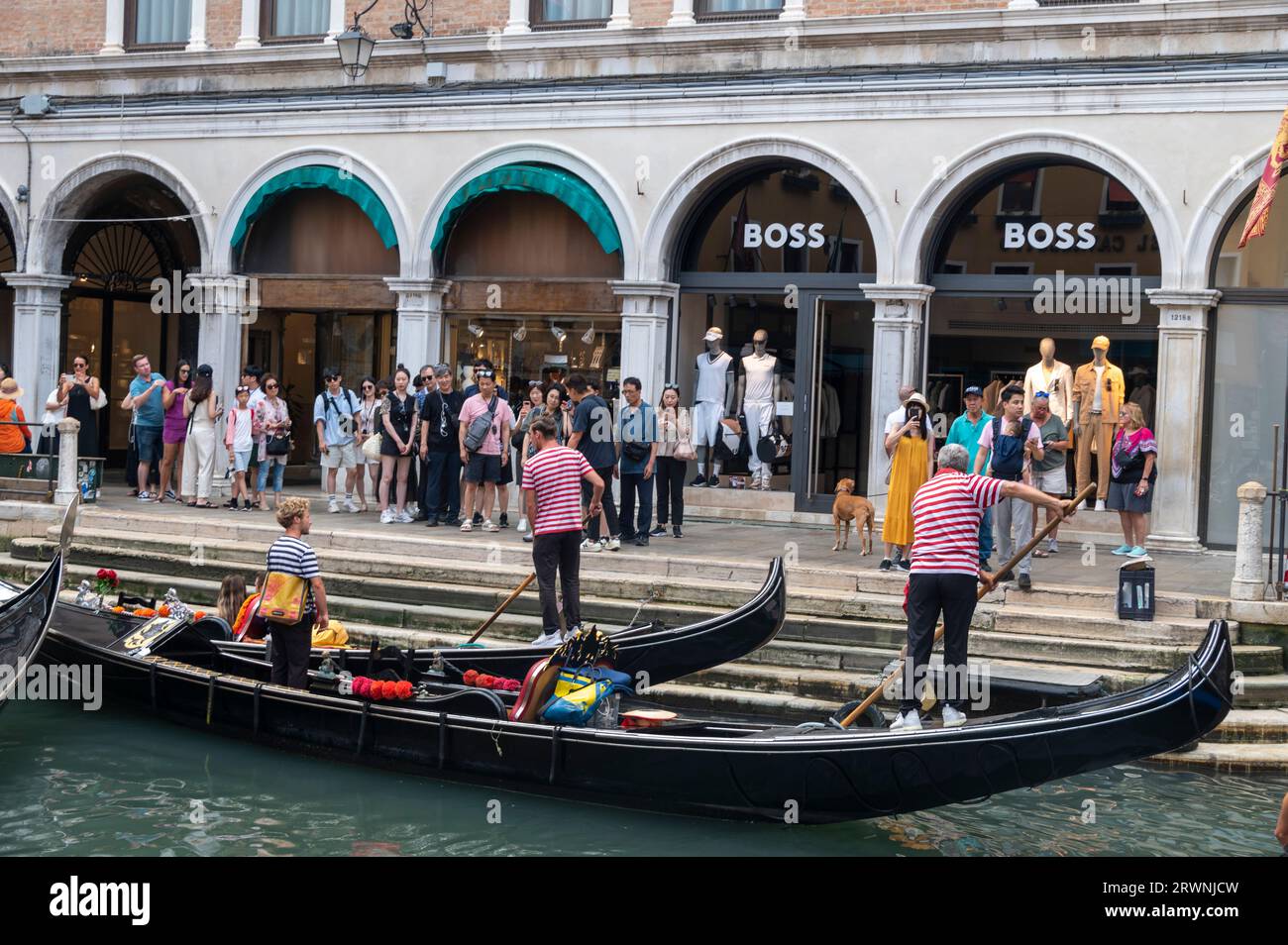A queue of tourists wait to board their gondolas for a tour at one of the official gondola stations based on the canals of Venice in the Veneto region Stock Photo