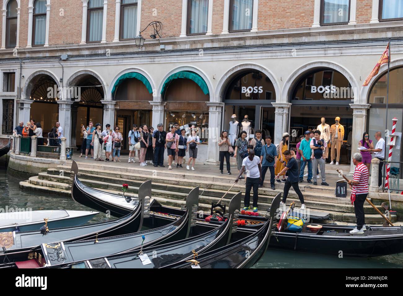 A queue of tourists wait to board their gondolas for a tour at one of the official gondola stations based on the canals of Venice in the Veneto region Stock Photo