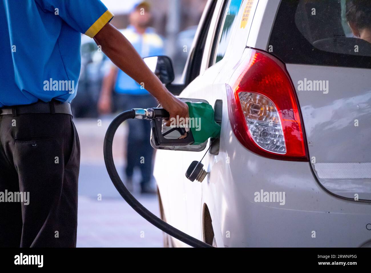 man manually filling fuel using a green nozzle into white car with