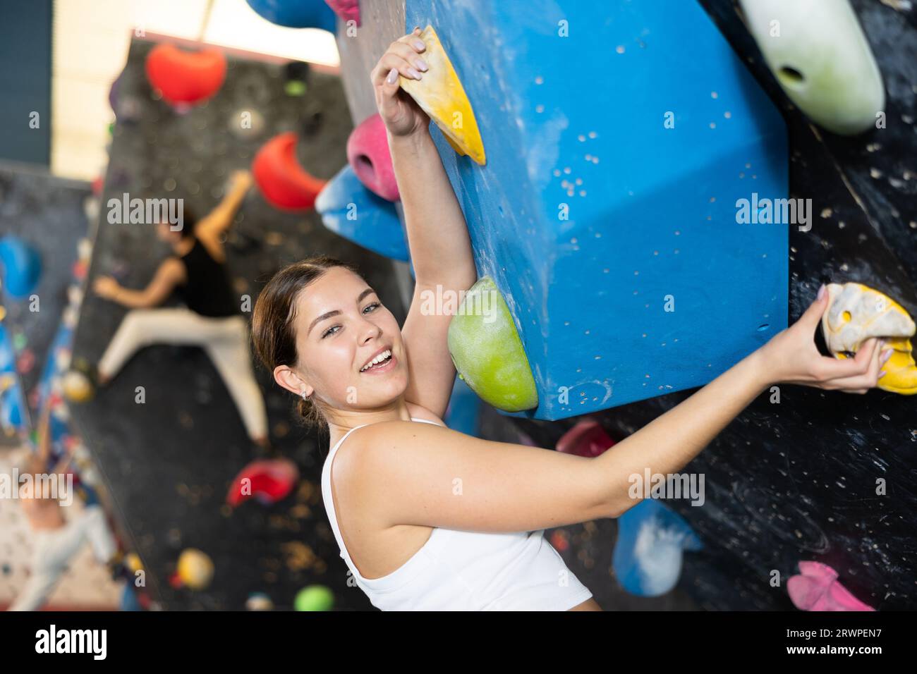 Beautiful young woman in black outfit climbing on practical wall in gym,  bouldering, extreme sport, rock-climbing concept. Stock Photo