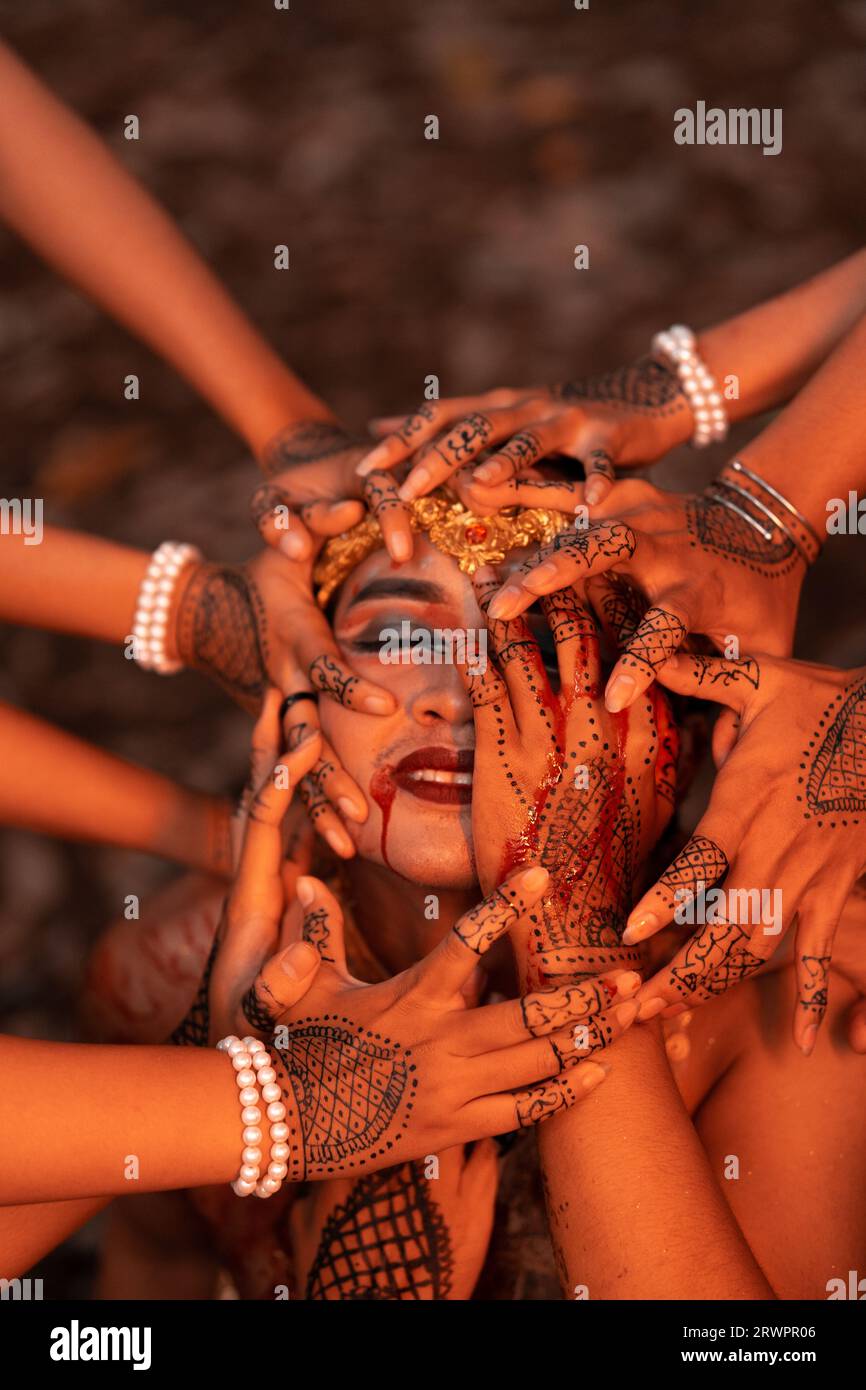 A Lot of hands holding an Asian man's face who had fake blood on her red lips like he was in pain in the forest Stock Photo