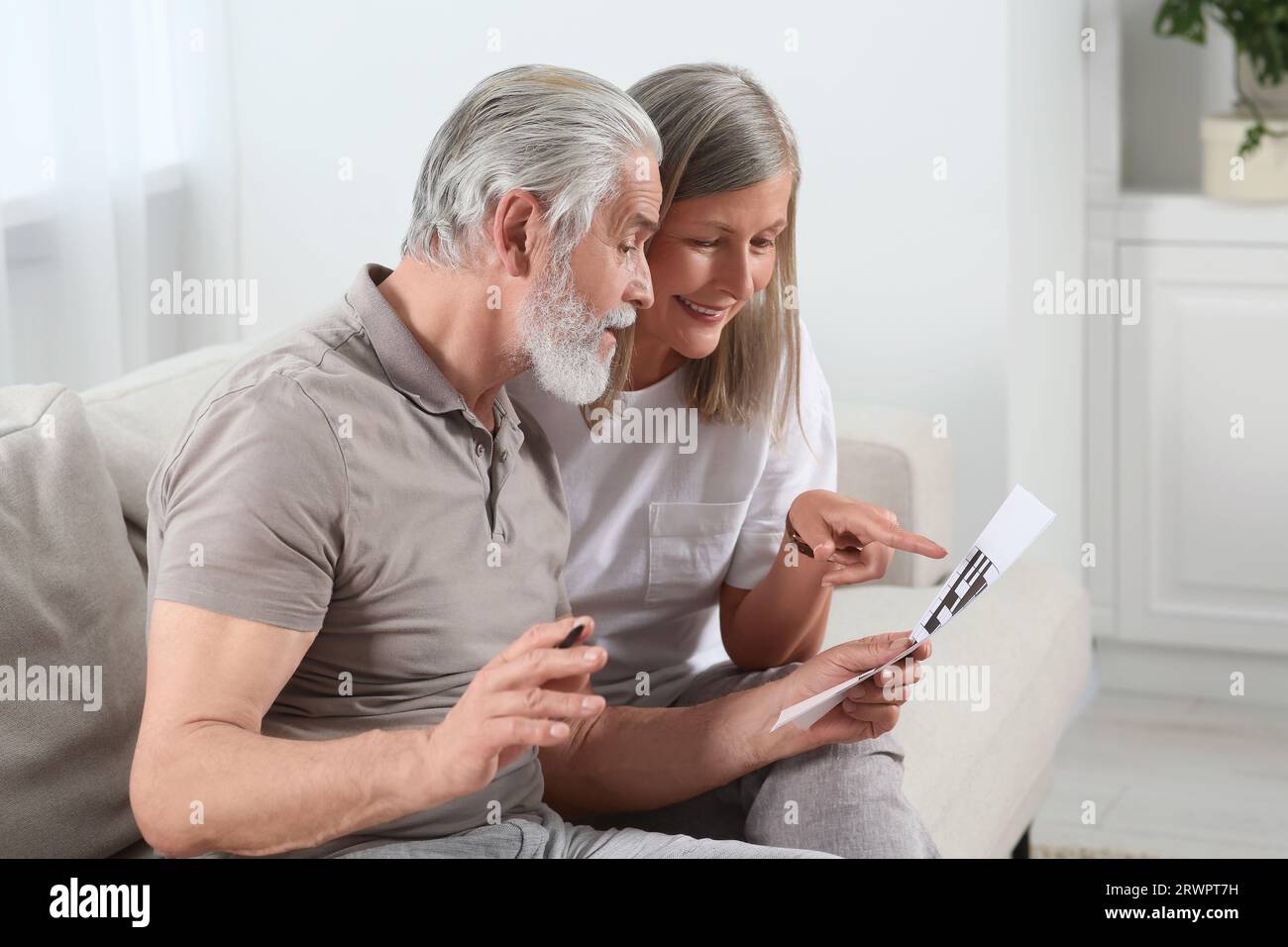 Senior couple solving crossword on sofa at home Stock Photo