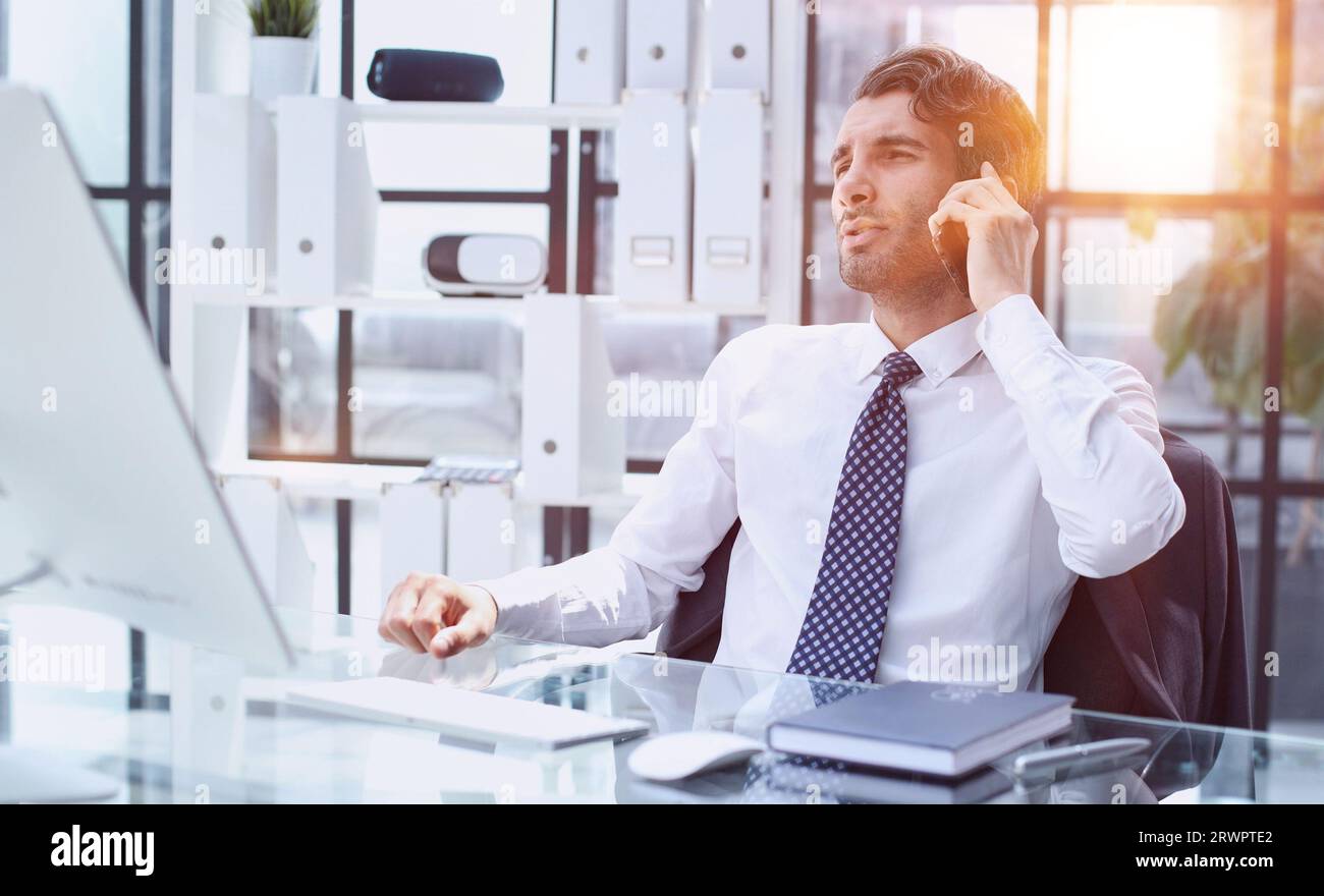 young web developer talking on phone while working with laptop in office Stock Photo