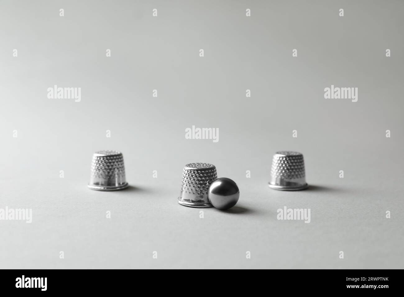 Metal thimbles and ball on light grey background. Thimblerig game Stock ...