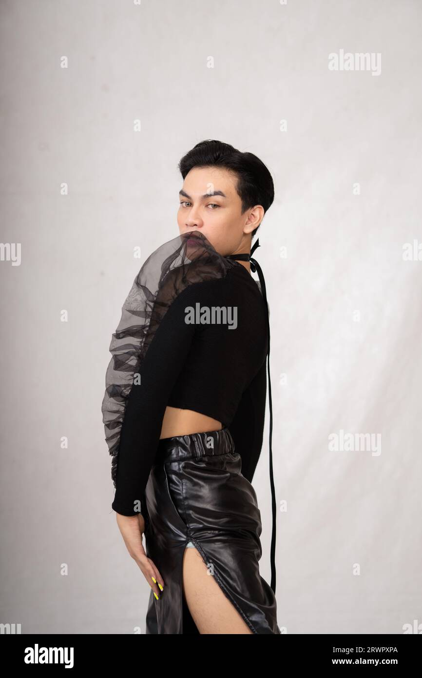 Asian man poses in a black costume while wearing makeup and black hair inside the studio Stock Photo