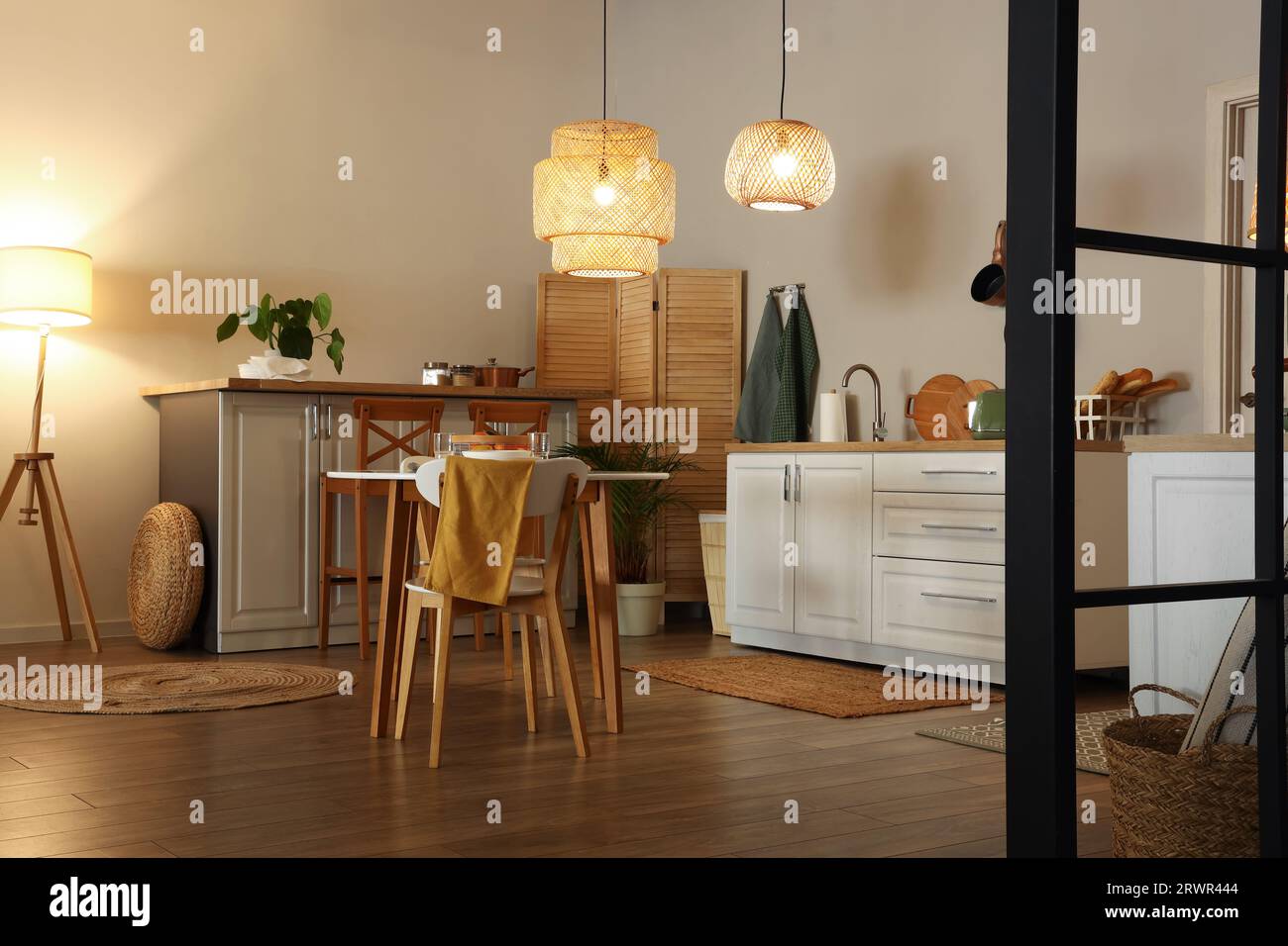 Interior of modern kitchen with glowing lamps, dining table and white ...