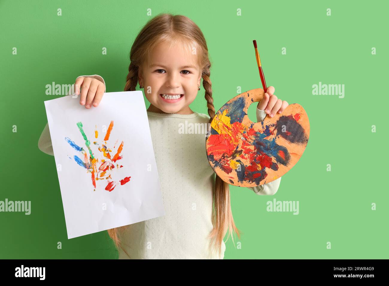 Cute little girl with drawing, paint palette and brush on green ...