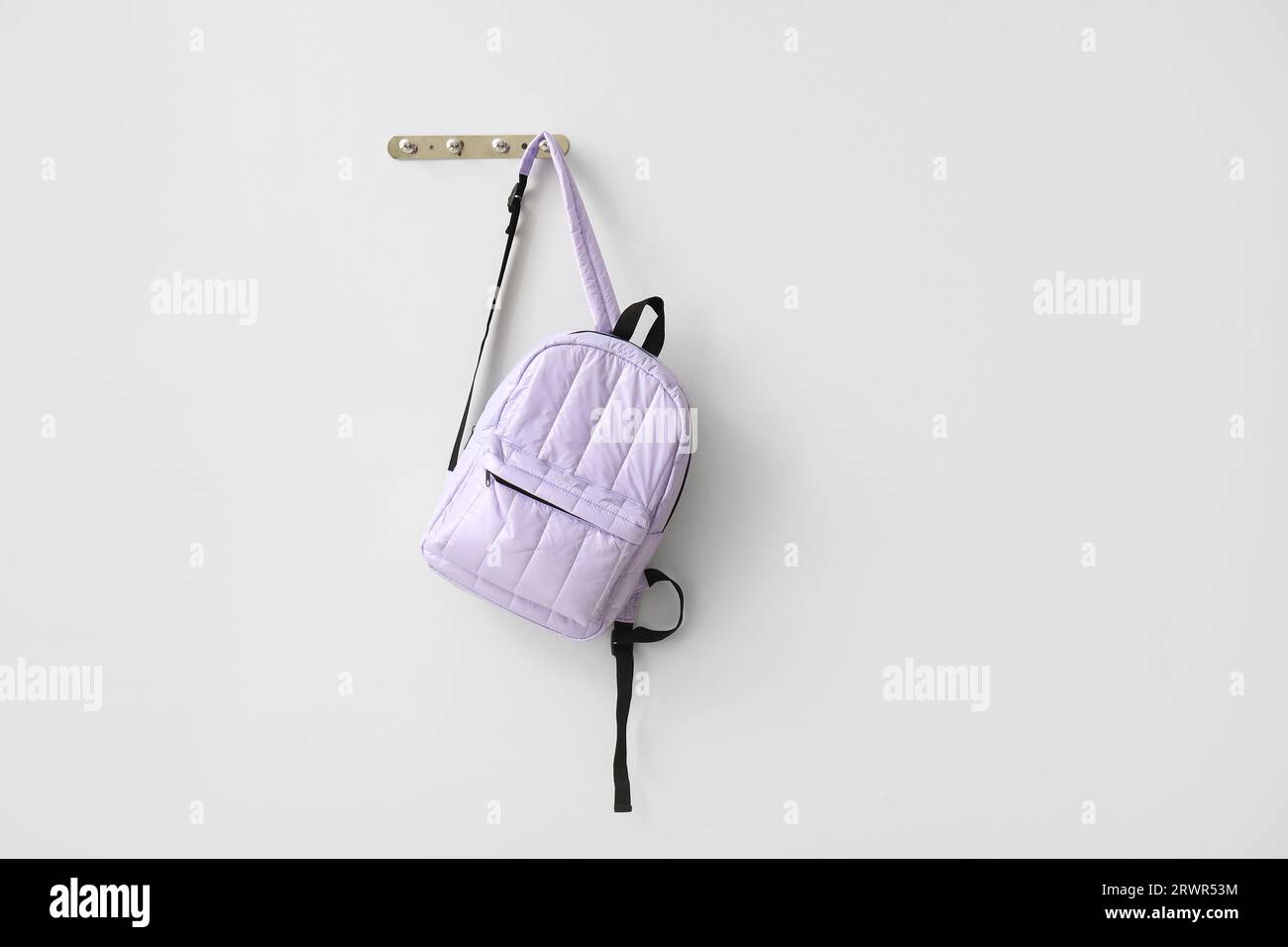 School backpack hanging on light wall Stock Photo