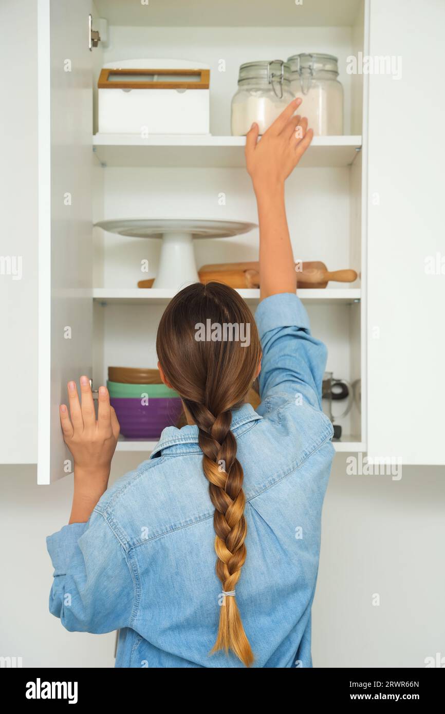 Woman opening kitchen cupboard with ingredients and set of kitchen