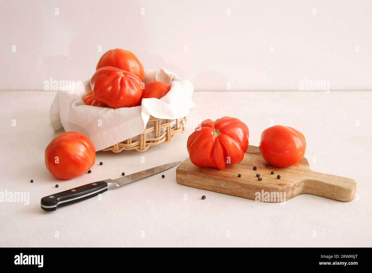 Wooden board and wicker bowl of fresh ripe tomatoes with peppercorn on ...