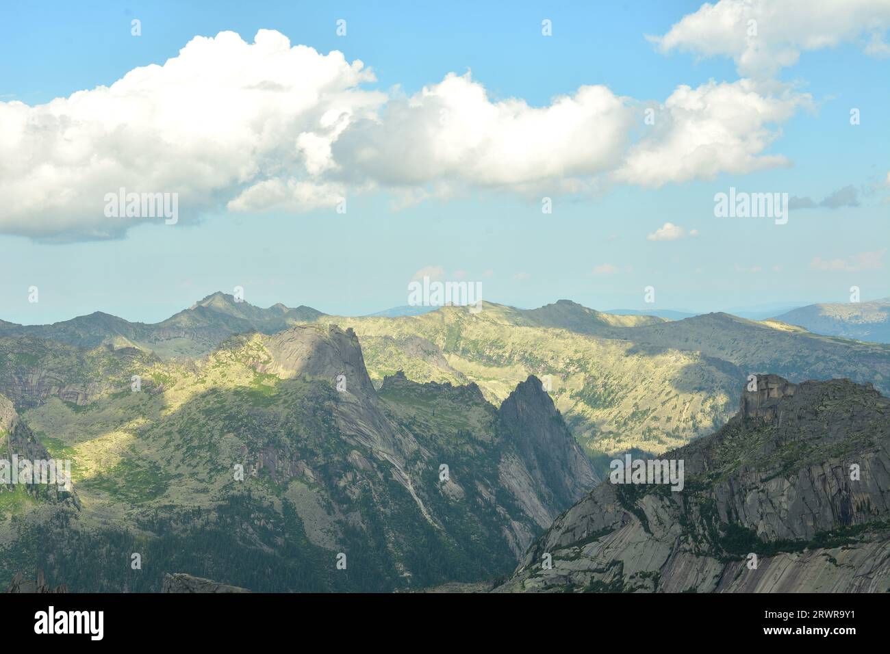 Thick cumulus clouds cast a shadow on a picturesque valley in the mountains with peaked peaks on a summer day. Natural park Ergaki, Krasnoyarsk region Stock Photo