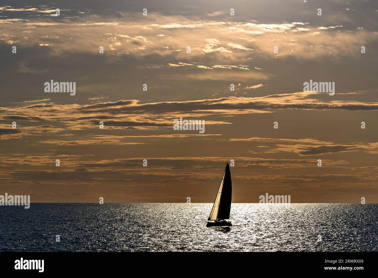 View of a sailing boat at sunset passing in front of the Artruxt Lighthouse, Cuidadela, Menorca, Balearic Islands, Spain Stock Photo