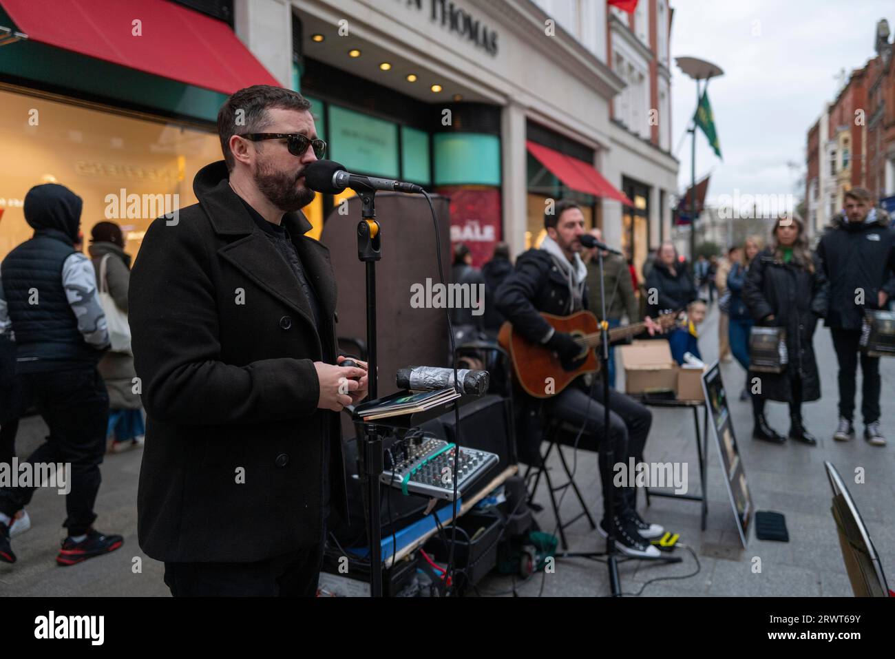 Andrew Kavanagh of Irish group Keywest singing in Grafton street with Andrew Glover in the back ground. Dublin, Ireland, Europe Stock Photo