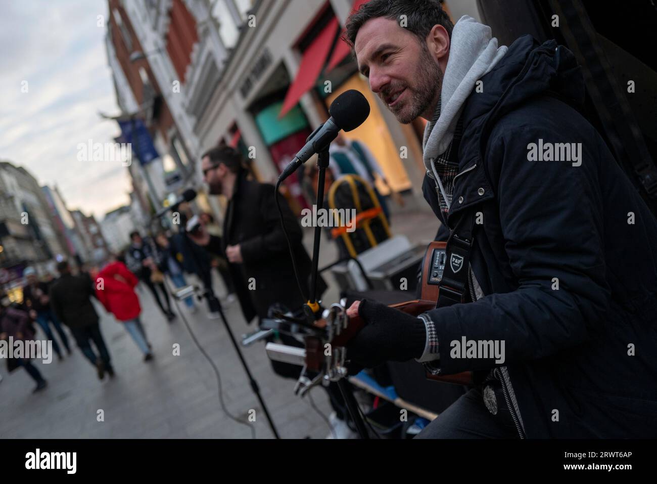 Andrew Glover of Irish pop group Keywest playing in Grafton Street with lead singer Andrew Kavanagh in the back ground. Dublin, Ireland, Europe Stock Photo