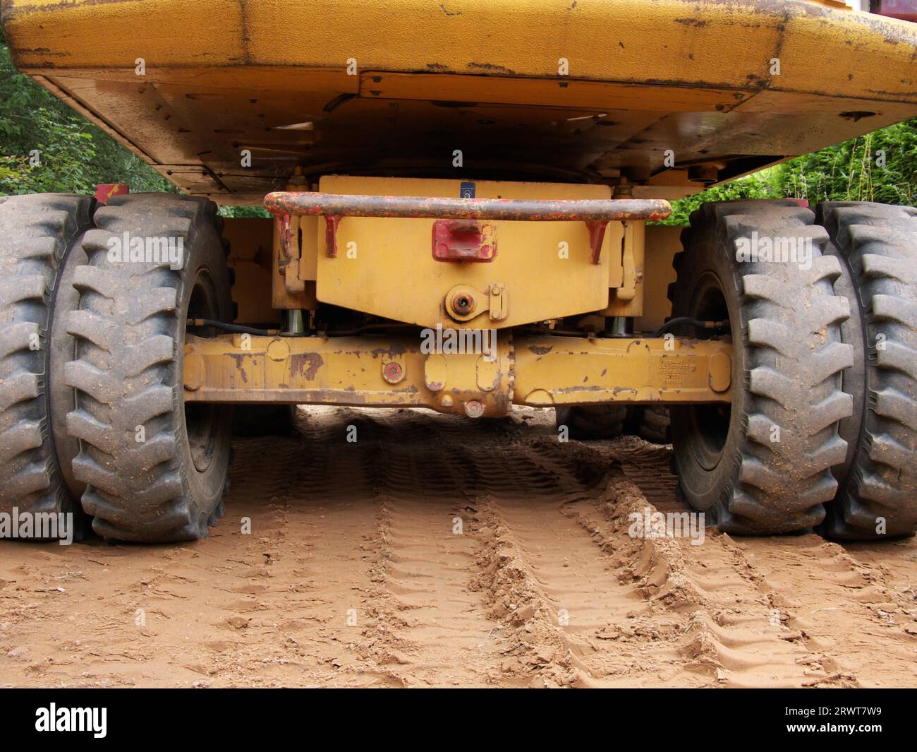 The back of an excavator standing on beige sand, tracks of the excavator underneath Stock Photo