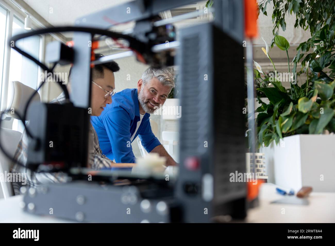 Two men architects using 3D printer in office and projecting house, drawing blueprints. Stock Photo