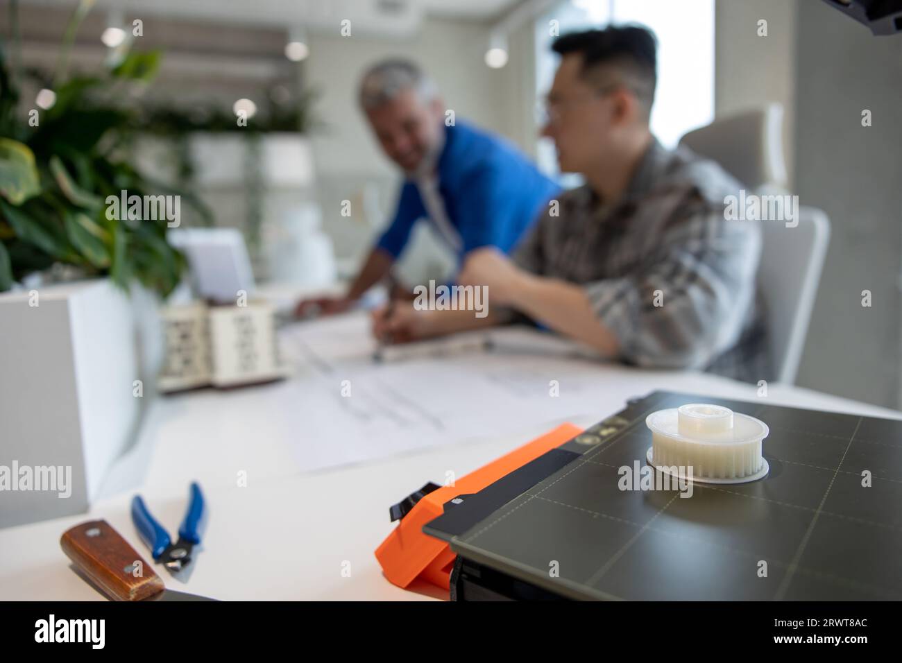 Two men architects using 3D printer in office and projecting house, drawing blueprints. Stock Photo
