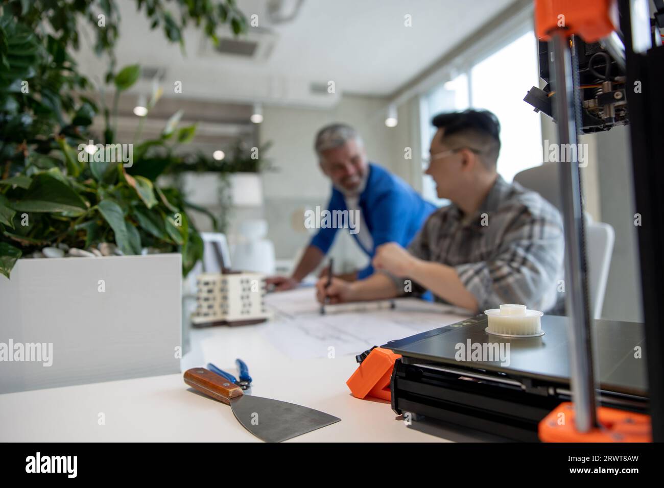 Two men architects using 3D printer in office and projecting house, drawing blueprints. Stock Photo