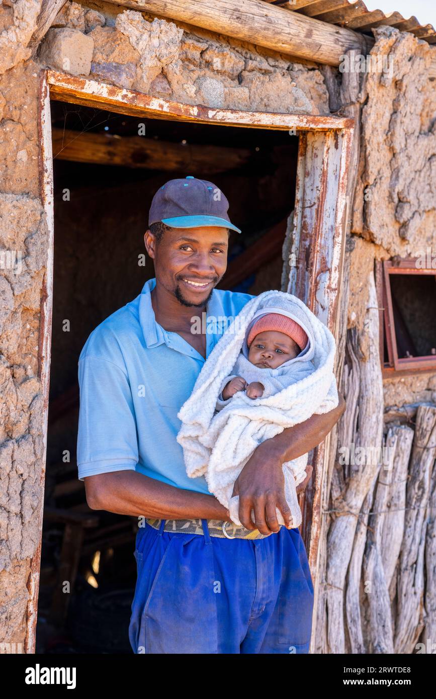 villager adult african man , single parent, holding his baby in front of the shack, village in Botswana, Stock Photo