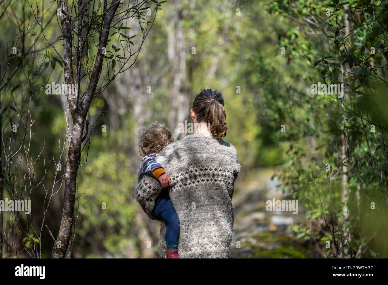 Mother with baby in a carrier on her chest on a hike, taking a bush