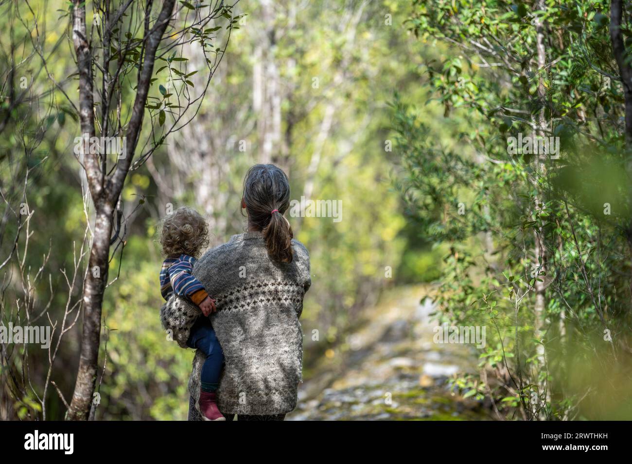 Mother with baby in a carrier on her chest on a hike, taking a bush