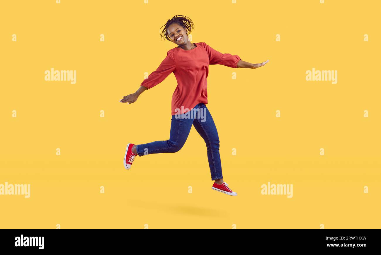 Happy cheerful young black woman in jeans jumping isolated on a yellow ...