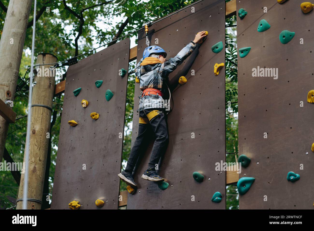 teenage boy climbing up the wall in outdoor adventure park passing obstacle course. high rope park Stock Photo