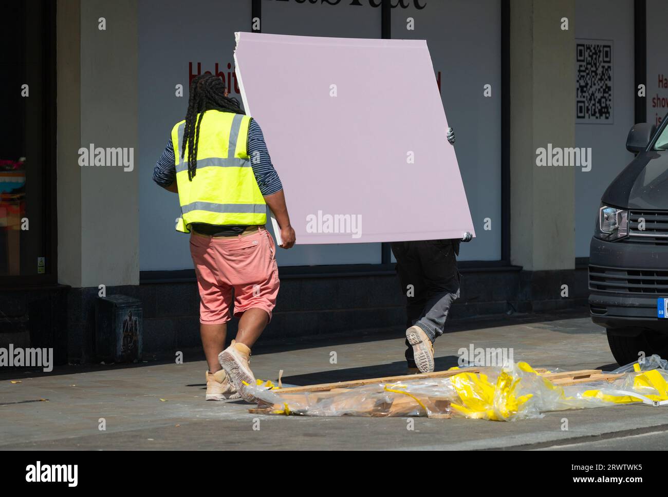 2 men making a delivery of goods in the UK, carrying a heavy item. Stock Photo