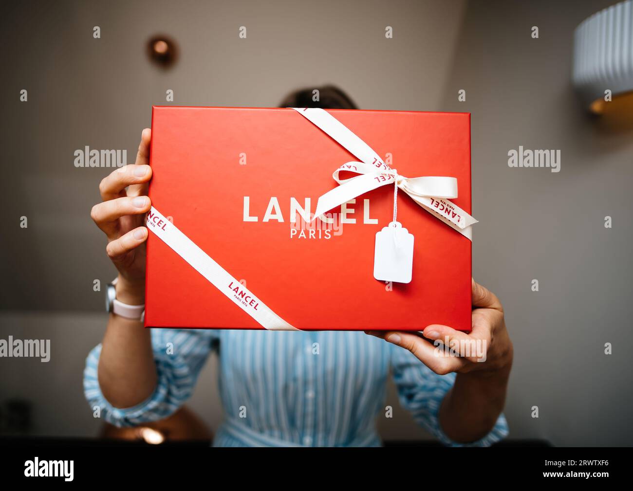 Paris, France - Aug 25, 2023: Captured in a luxurious interior, a frontal view of a woman elegantly holding a red cardboard gift from Lancel fashion brand dominates the frame. Stock Photo