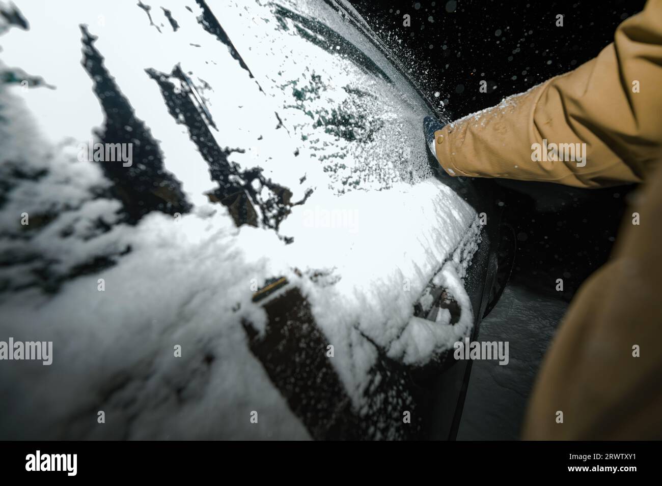 Captured against the night's darkness, a male hand in a glove carefully removes snow from the frozen windows of a car following a severe tempest Stock Photo