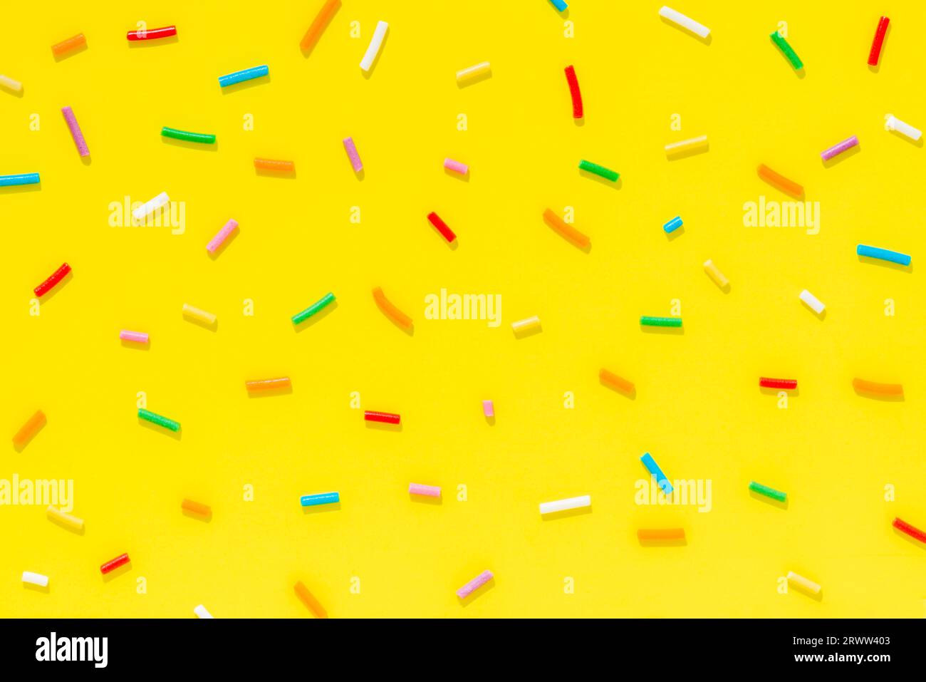 flat lay of colorful sprinkles over yellow background, festive decoration for banner, poster, flyer, card, postcard, cover, brochure, designers. Stock Photo