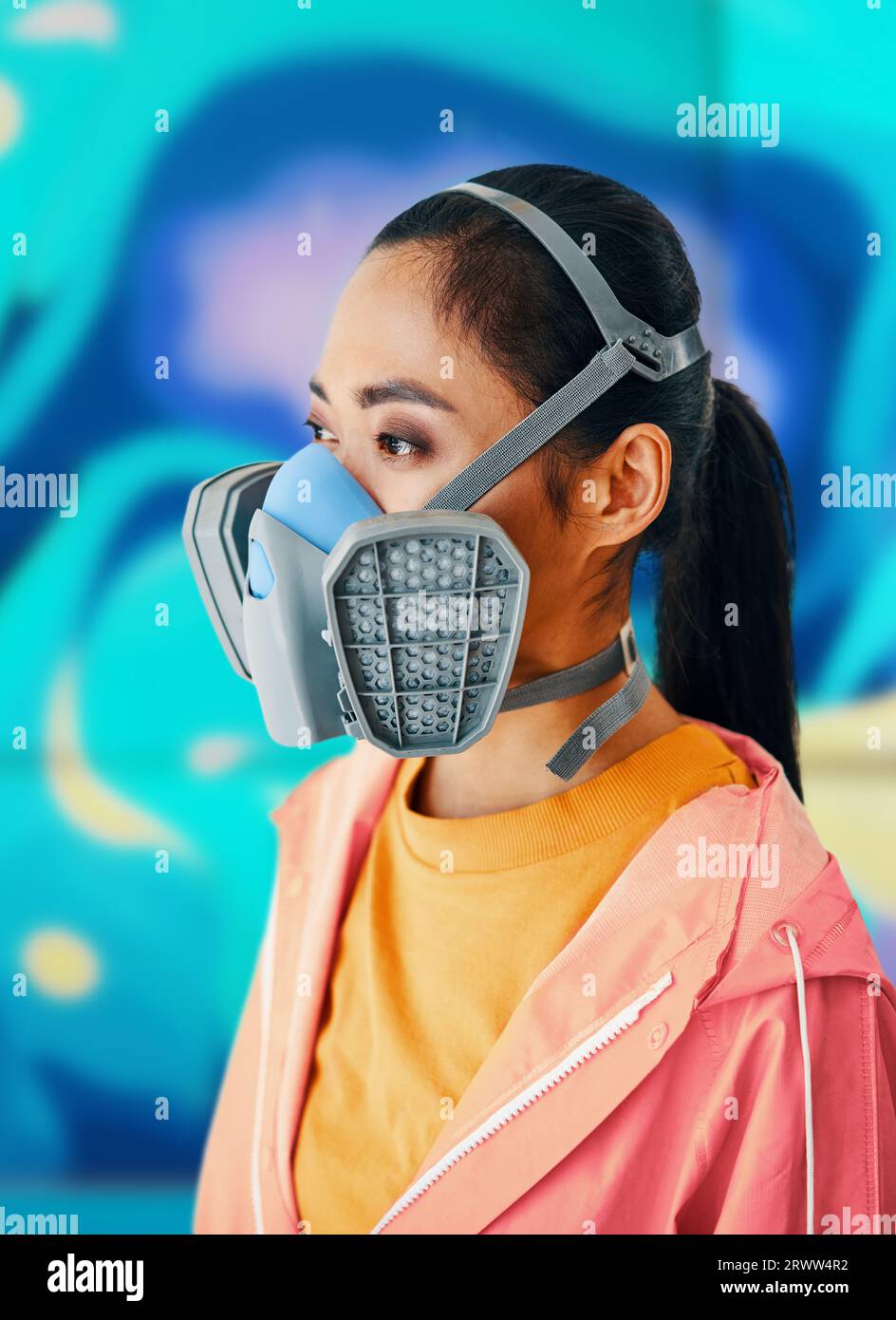Close up portrait of graffiti street artist in respirator mask standing near the wall with her colorful paintings. Urban art concept Stock Photo