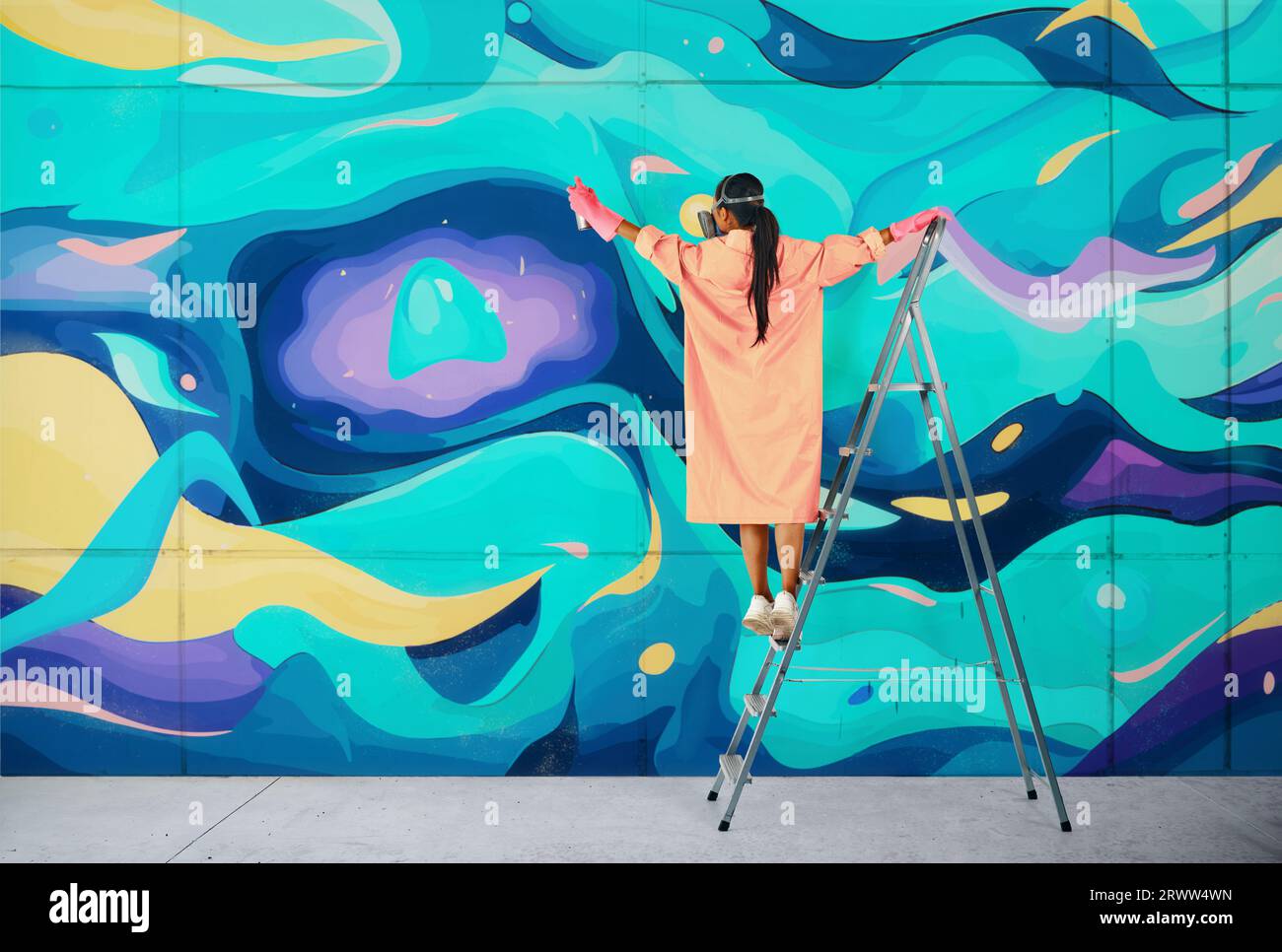 Female street artist painting colorful graffiti standing on a ladder. Modern art, urban concept. Stock Photo