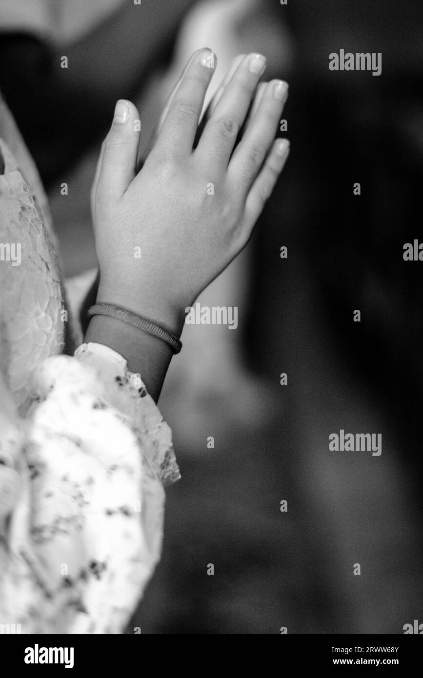 A grayscale shot of a young girl standing with her hands together in a