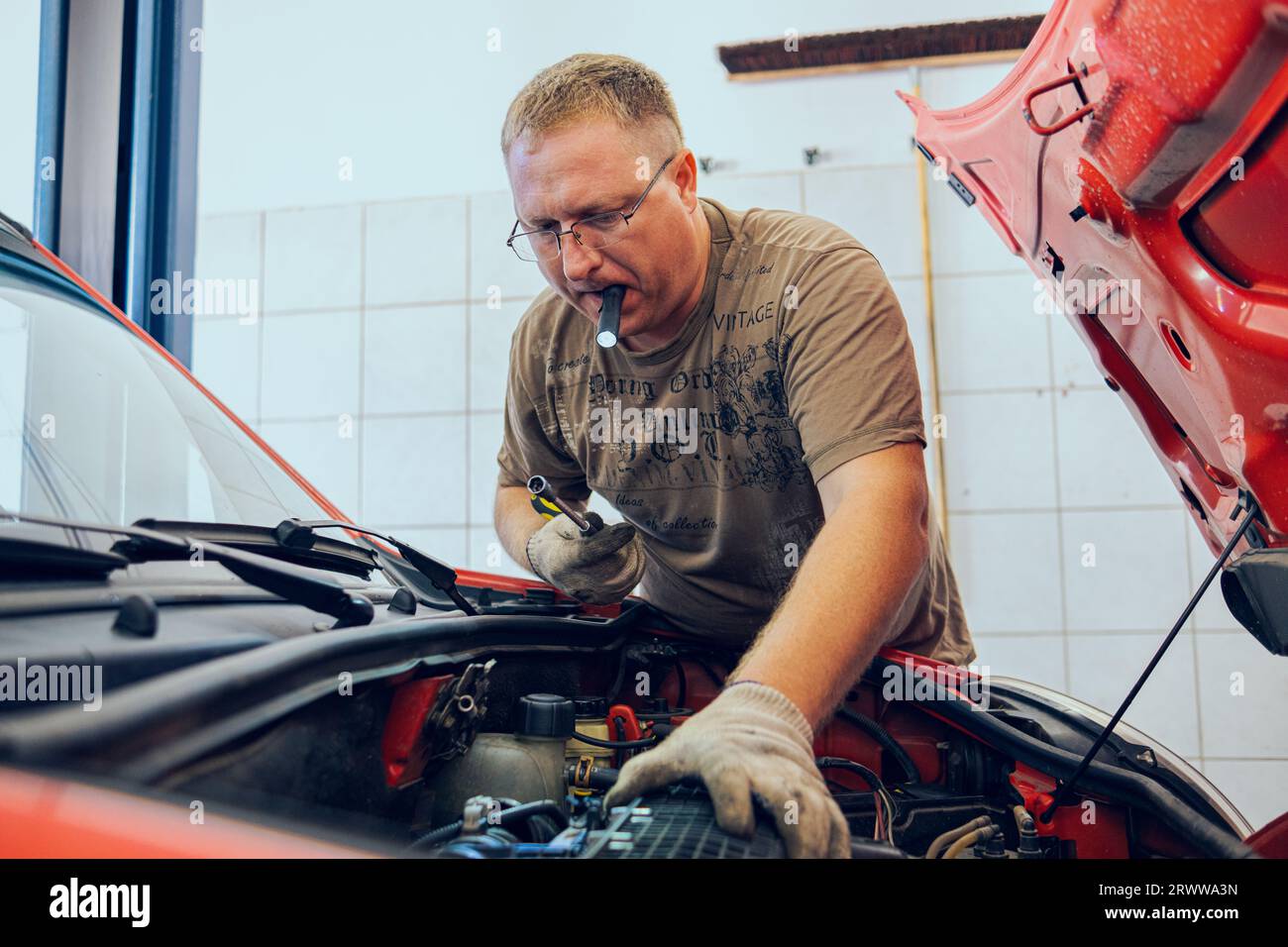 A Man with glasses Maintains a Car in a Garage. Car Repair by an experienced Specialist in a Car Repair Shop. Replacing the oil and filter in the car. Stock Photo