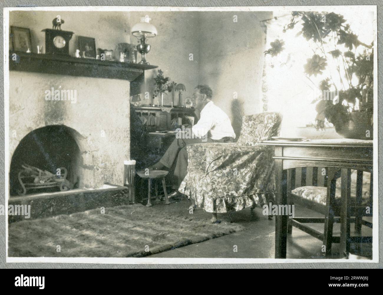 One of a series of five photos showing the interior of the Bungeys' Kabete sitting room, with large fireplace, writing desk, table and chairs. This image shows Charles Bungey sitting at the writing desk. A dog is asleep in front of the fireplace.  Original manuscript caption: Interior of Sitting Room, Kabete 1924. Stock Photo